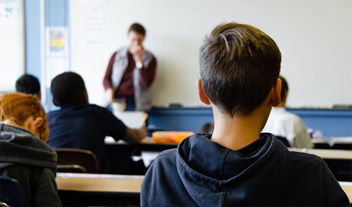 Elev i klassrum. En suddig lärare står framför klassen.