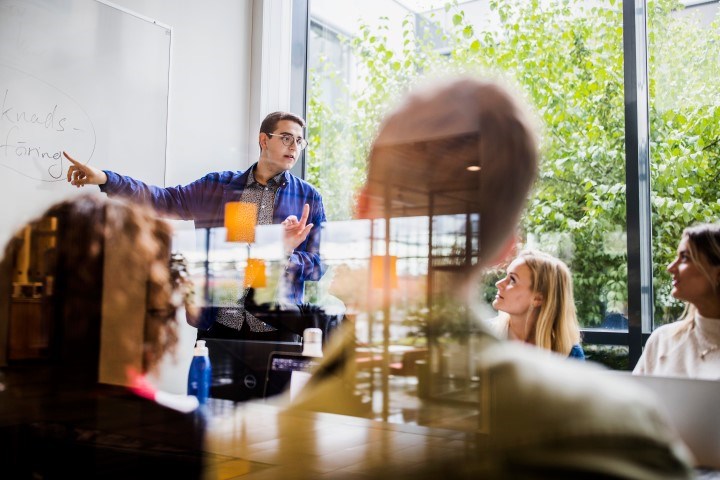 Student som pekar på whiteboard framför andra studenter