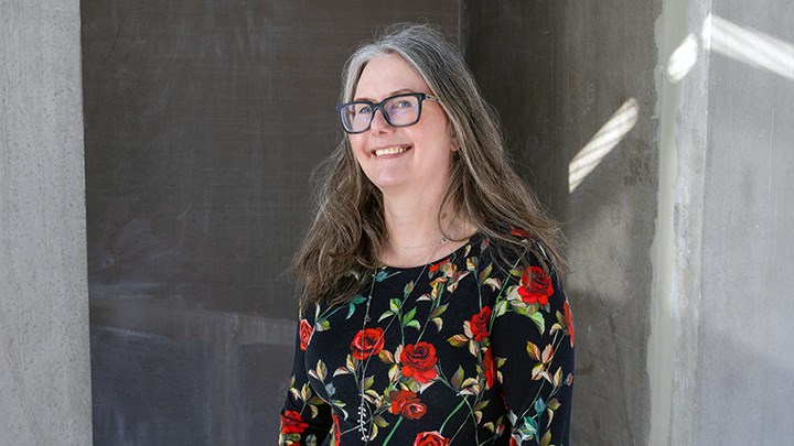 Karin Hedström, wearing a floral dress, stands in front of a grey wall.