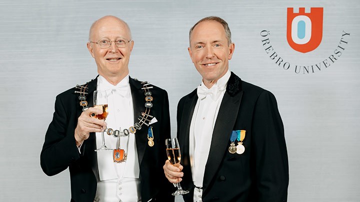 Rektor och Mattias på akademisk högtid framför en fotoskärm.