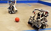 Två robotar som spelar fotboll med en liten röd boll.