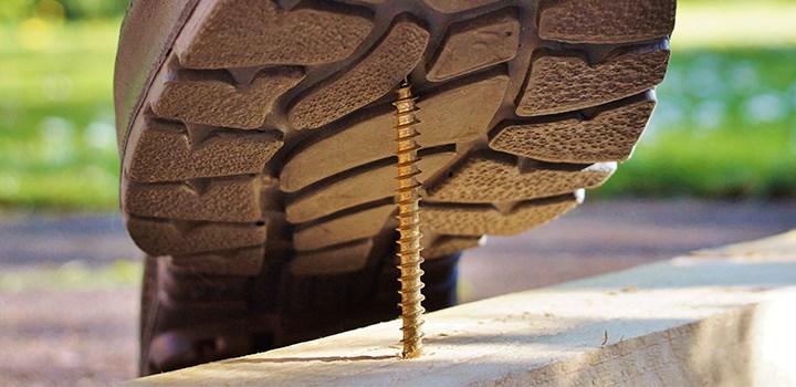A shoe stepping on a screw sticking up through a piece of wood.