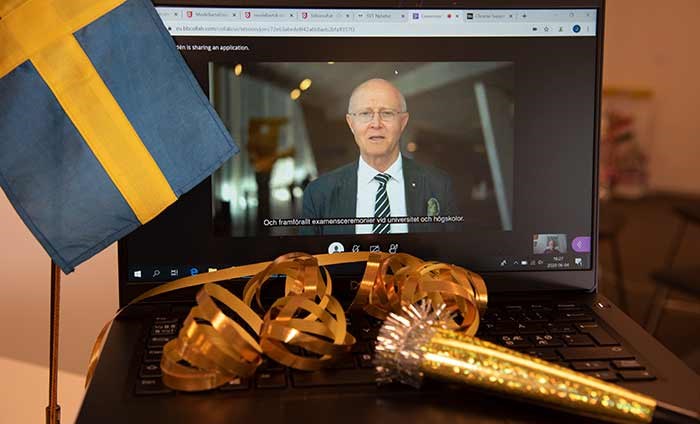 Rektor Johan Schnürer på en datorskärm med svenska flaggan och serpentiner framför. 