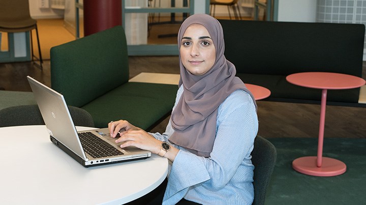 Foto på person som sitter med en dator vid ett bord.