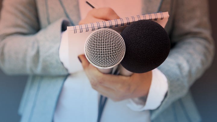 A journalist writing on a notepad and holding two microphones