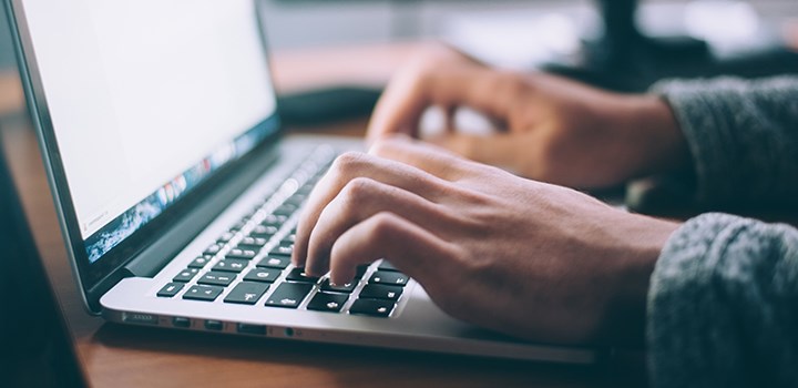 Photo of two hands typing on a laptop keyboard.