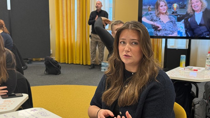 En student diskuterar i gruppen med lärare och tv i bakgrunden.