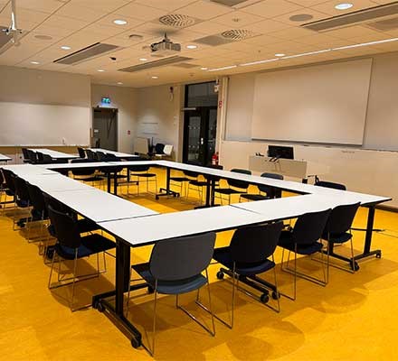 Vy X4423 Bord och stolar möblerade i ett U. Ett teknikbord syns också.