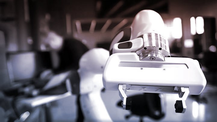 Close-up of a robotic arm in a laboratory setting with a person in the background of Robotlab