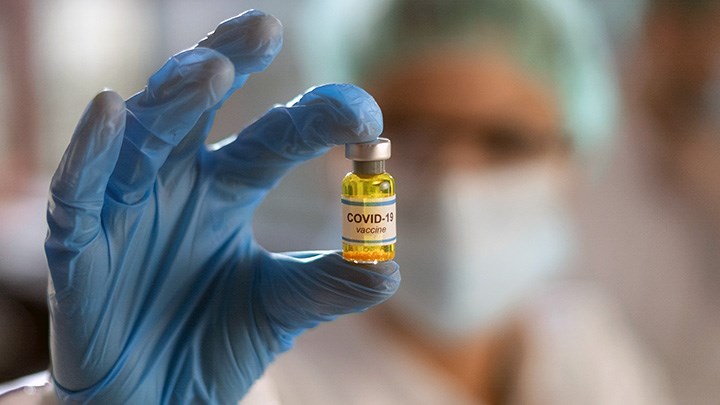 Foto på en hand som håller i en liten flaska med texten "Covid-19 vaccine" på