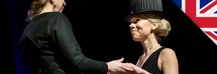 Två kvinnor i svarta kläder och svarta doktorshattar håller varandra i händerna. De tittar på varandra.