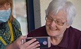 Vårdpersonal visar någonting på en mobil för en äldre kvinna. 