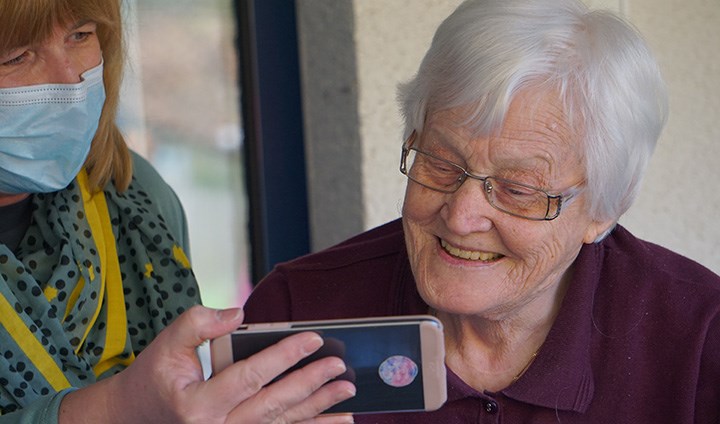 Vårdpersonal visar någonting på en mobil för en äldre kvinna. 