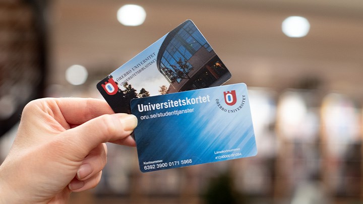 Photo of a hand holding a university card and a library card.