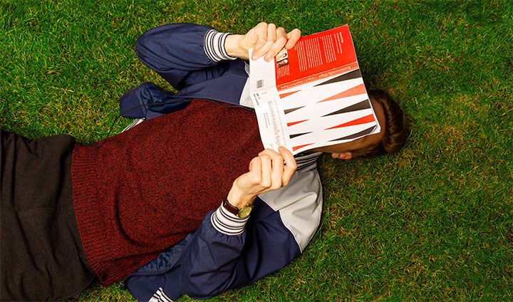 En person ligger på en gräsmatta och läser en bok
