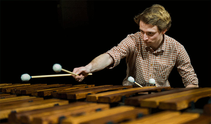 Man playing a percussion instrument with two hand-held beaters in each hand.