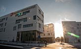 The sun is making an appearance between Örebro University’s white buildings. In the foreground is the Nova building, with a large Örebro University sign on the façade.