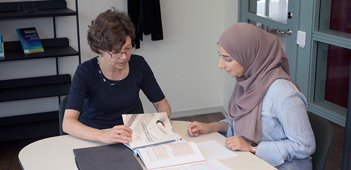 Photo of two people sitting by a table and studying a book.