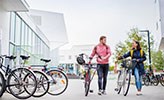 Två studenter leder sina cyklar på campus.