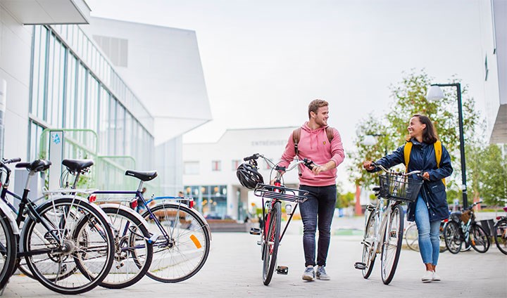 Två studenter leder sina cyklar på campus.