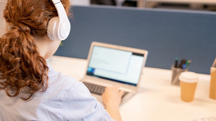 Foto på en person med hörlurar som sitter vid en dator.