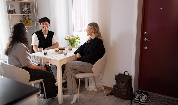 Tre studenter sitter och fikar i en lägenhet.