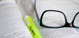 Foto på en uppslagen bok med en gul överstrykningspenna och ett par glasögon.