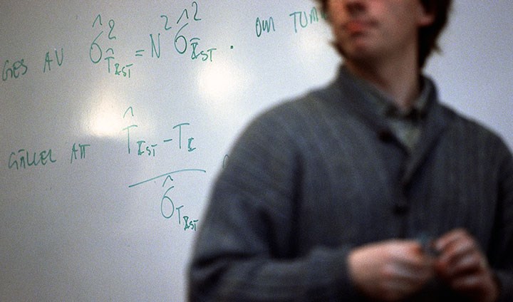 Foto på en person som står framför en whiteboard med olika matematiska uträkningar.