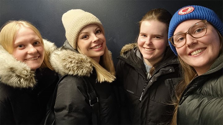 Four smiling students in winter clothes outside in the snow.