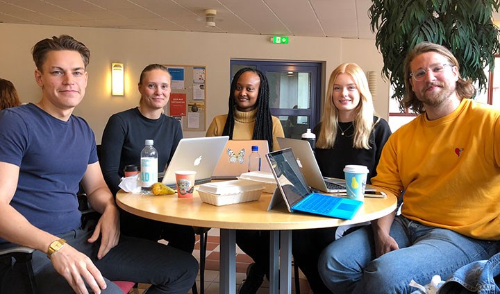 Fem studenter som arbetar tillsammans sittandes runt ett bord. 