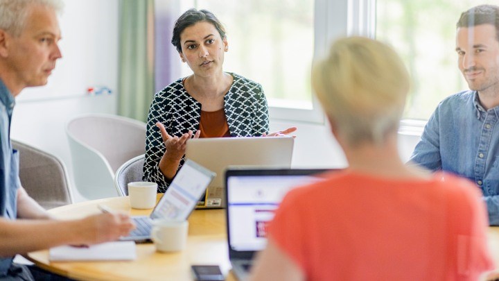 Fyra personer sitter med datorer och jobbar runt ett bord.