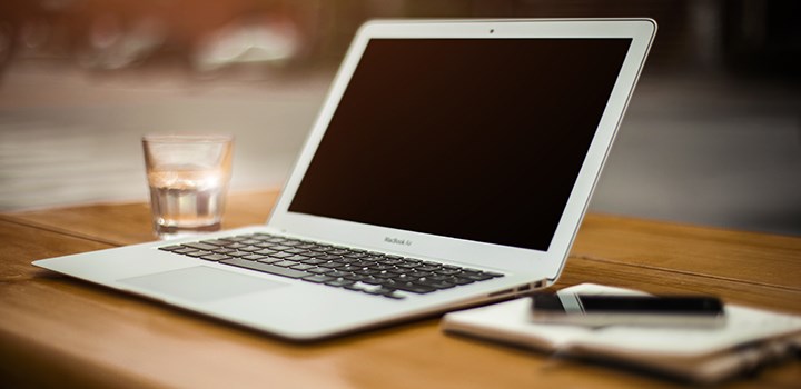 A photo of a laptop, a glas of water and a note pad.