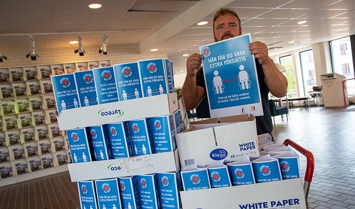 En man håller upp en affischmed texten "Här får du vara extra försiktig". På en vagn står hundratals bordspratare med samma budskap.