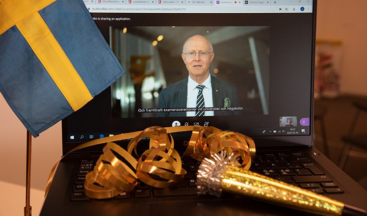 En datorskärm med rektor som håller tal. På tangentbordet ligger serpentiner och en guldtuta. En liten svensk flagga syns i vänsterkant.