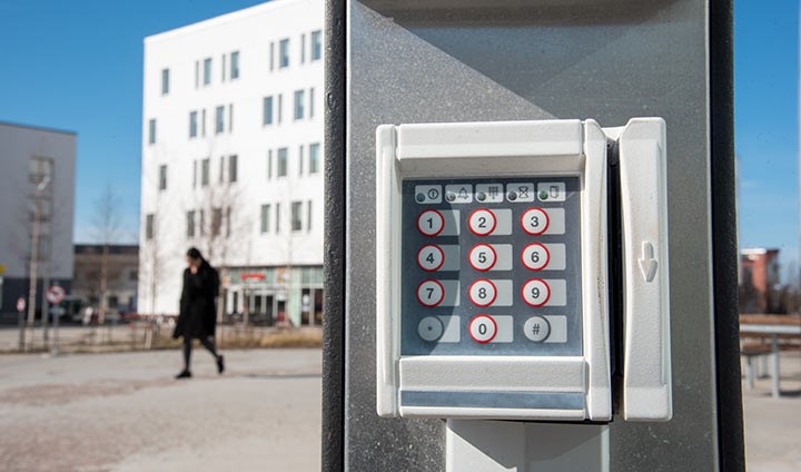 En kortläsare i förgrunden. I bakgrunden syns vita hus på universitetsområdet.