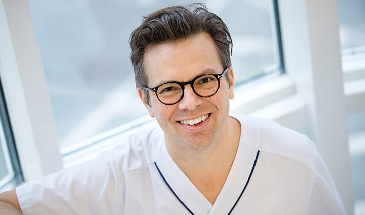 Porträttbild på en leende Jonas Halfvarson i vita sjukhuskläder.