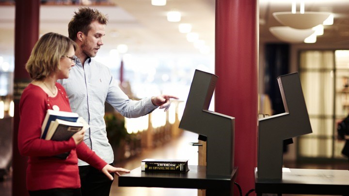 Två personer står vid en bildskärm i biblioteket.