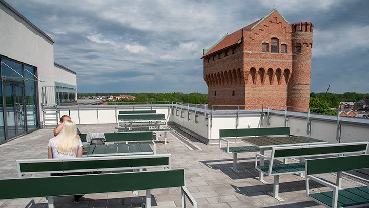 En takterass med görna träbänkar och bord. I bakgrunden syns ett vattentorn byggt av tegel.