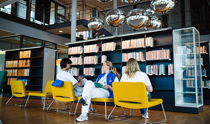 Tre personer sitter på gula stolar i biblioteket på Campus USÖ.