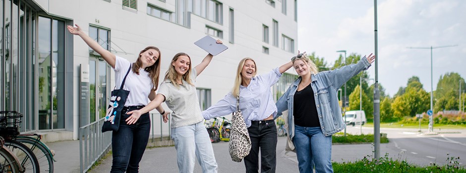 Fyra studenter står utomhus med armarna utsträckta och tittar in i kameran.