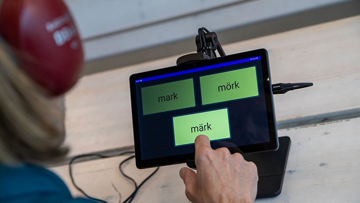 A person wearing headphones and pointing to one word among three on a tablet.