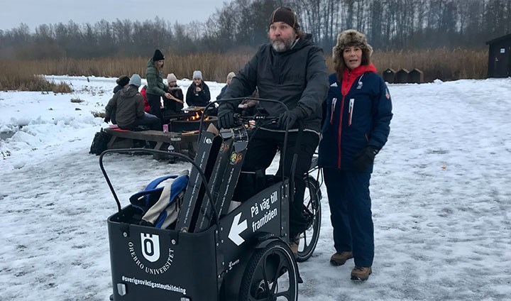 Två personer vid en lådcykel. I bakgrunden syns studenter runt en lägereld.