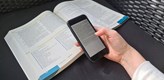 Foto på en mobiltelefon som en person håller ovanför en uppslagen bok.