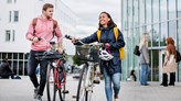 Två studenter går med sin cyklar framför Prismahuset.