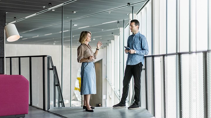 A woman and a man are talking to each other on a staircase by large windows.
