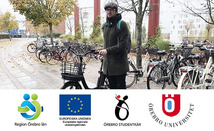 Robert Högg står med en svart cykel på campus bredvid ett cykelställ. 