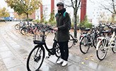 Robert Högg står med en svart cykel på campus bredvid ett cykelställ. 