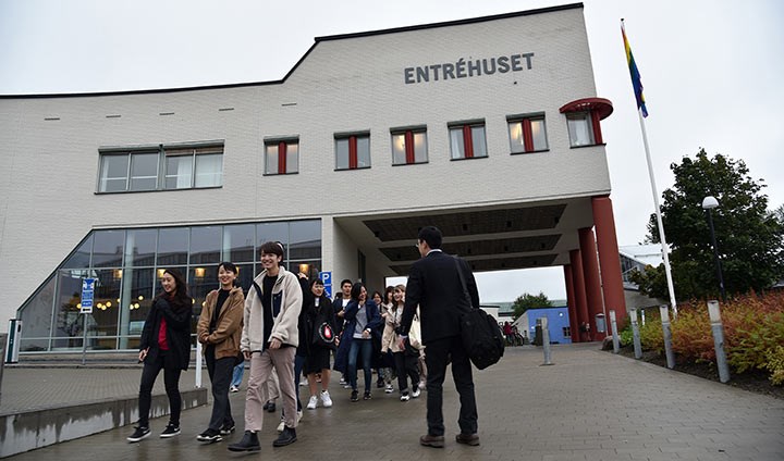 Studenter och lärare från Yokohama går framför en vit byggnad som det står ”Entréhuset” på. Studenterna skrattar och har roligt.