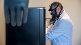 En man i skyddsmask står med händerna inne i en SLS-printer, en 3D-printer.
