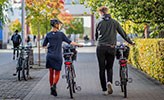 En man och kvinna leder varsin cykel på campus. 